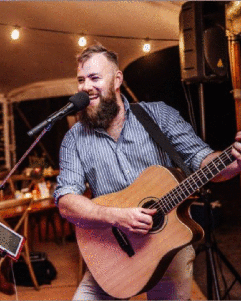 Troy Elliott smiling while playing guitar during live music session at The Courthouse Hotel