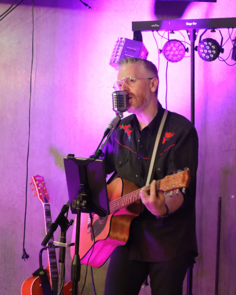 Adam Cameron performing live on guitar with mic and soft purple lighting